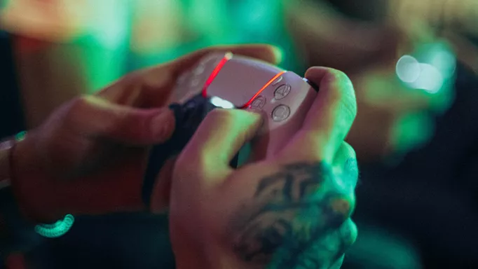 A player holds the PlayStation 5 DualSense controller as its lighting glows red.