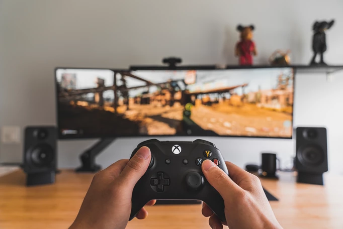 A player using an Xbox controller to play a game on an ultra-wide monitor.